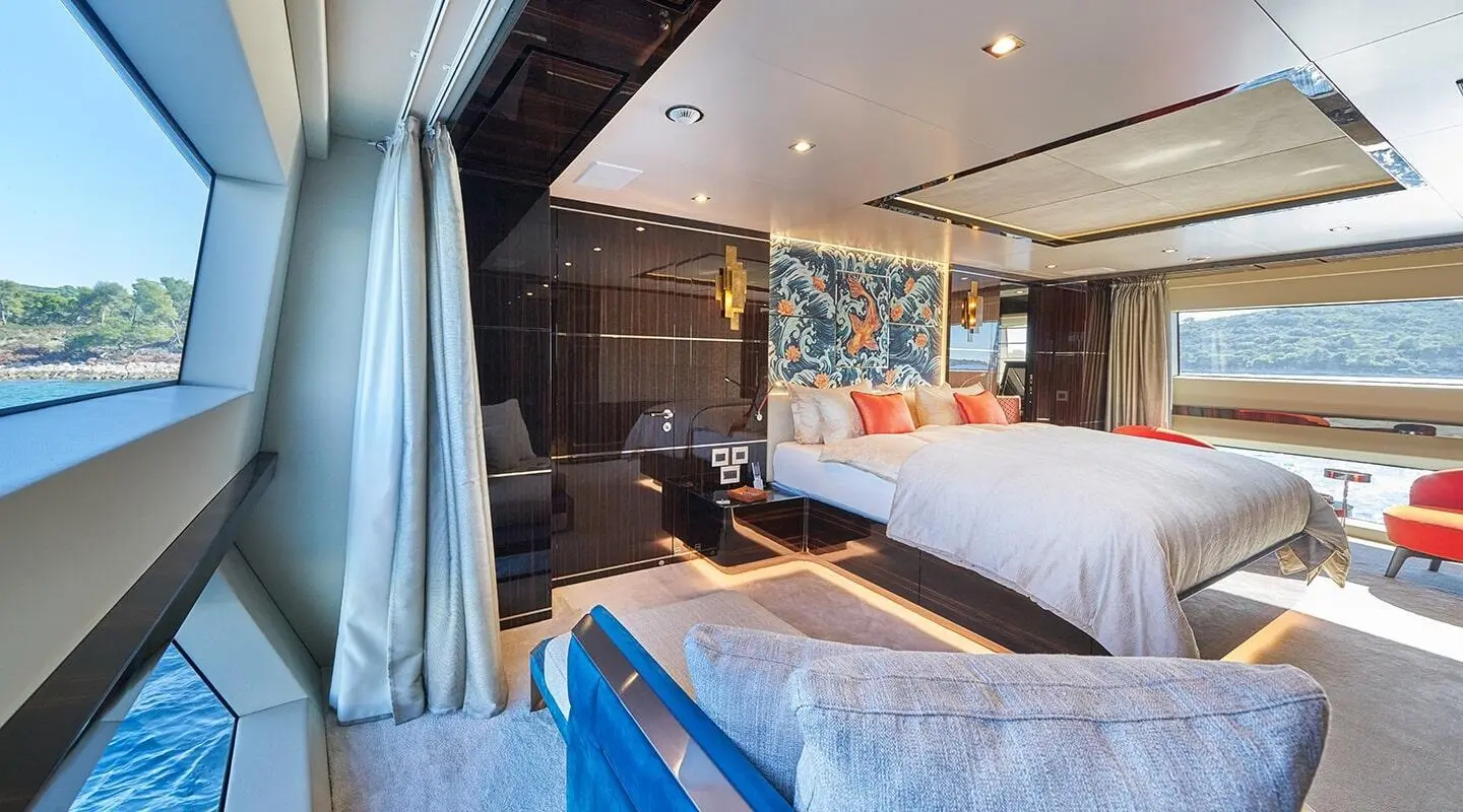 Interior of a luxury yacht cabin with a bed, seating, and blue curtains