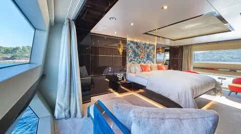 Interior of a luxury yacht cabin with a bed, seating, and blue curtains