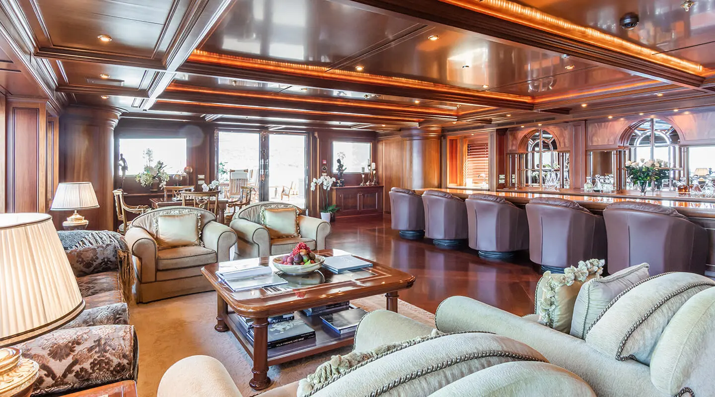 Luxurious wood-paneled salon with sofas and a coffee table; bar area in the background