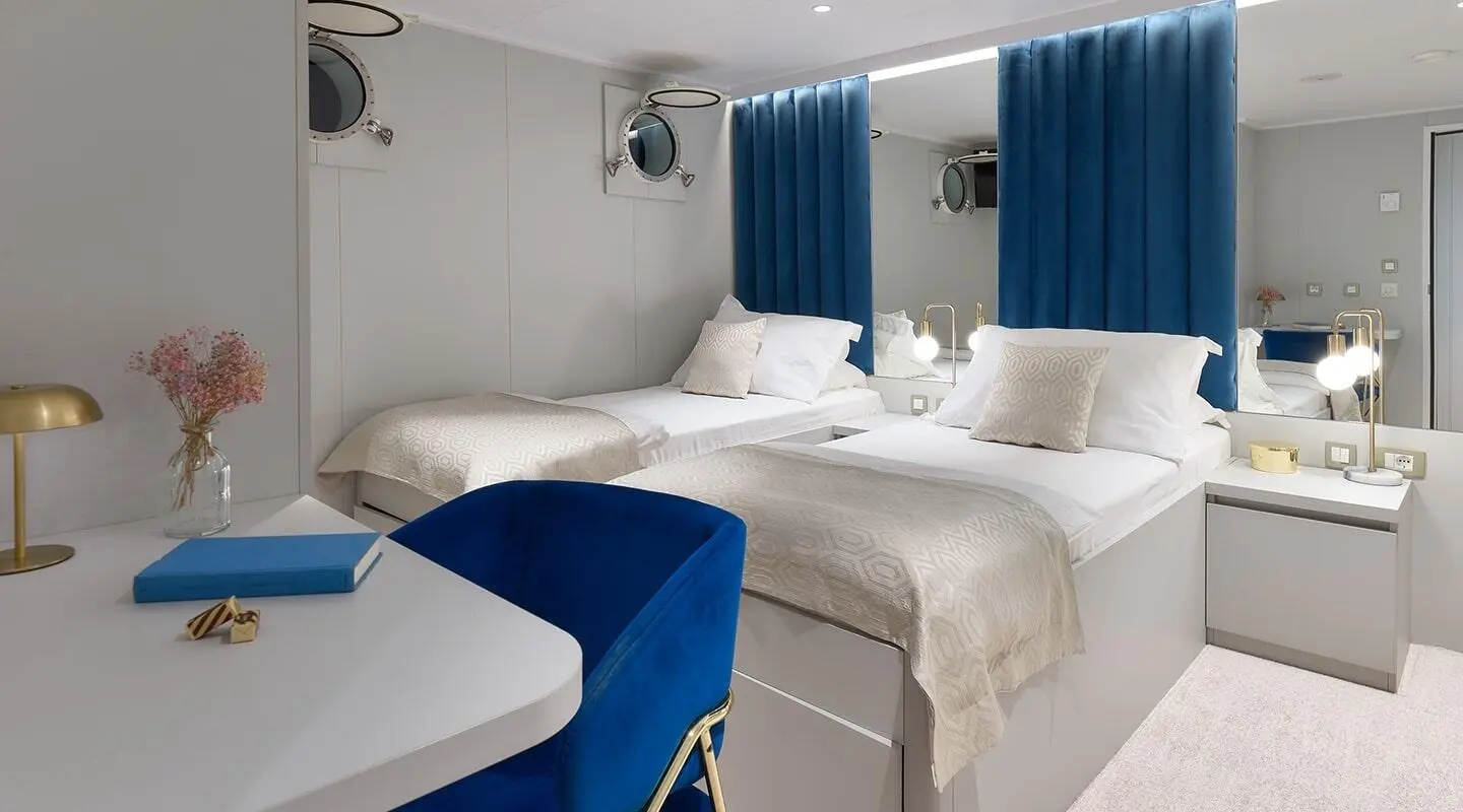 Interior of a yacht cabin with two beds, blue accents, and white linens