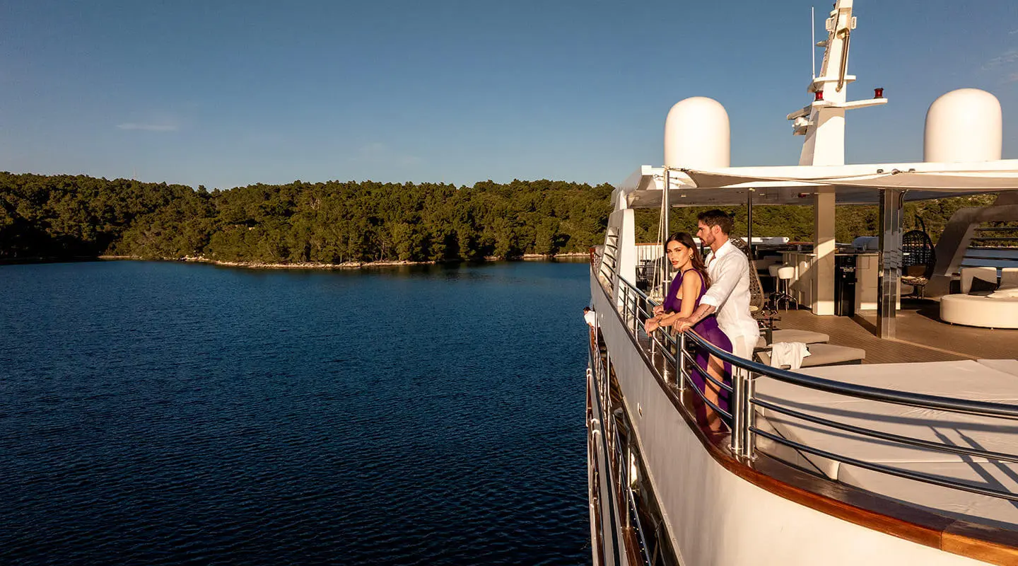 People on the yacht Cristal's sun deck overlooking calm blue water and shoreline