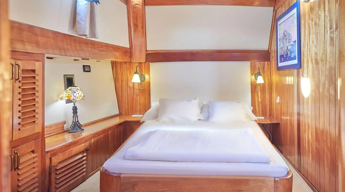 Libra yacht cabin with polished wood paneling and white bedding in elegant luxury ambiance