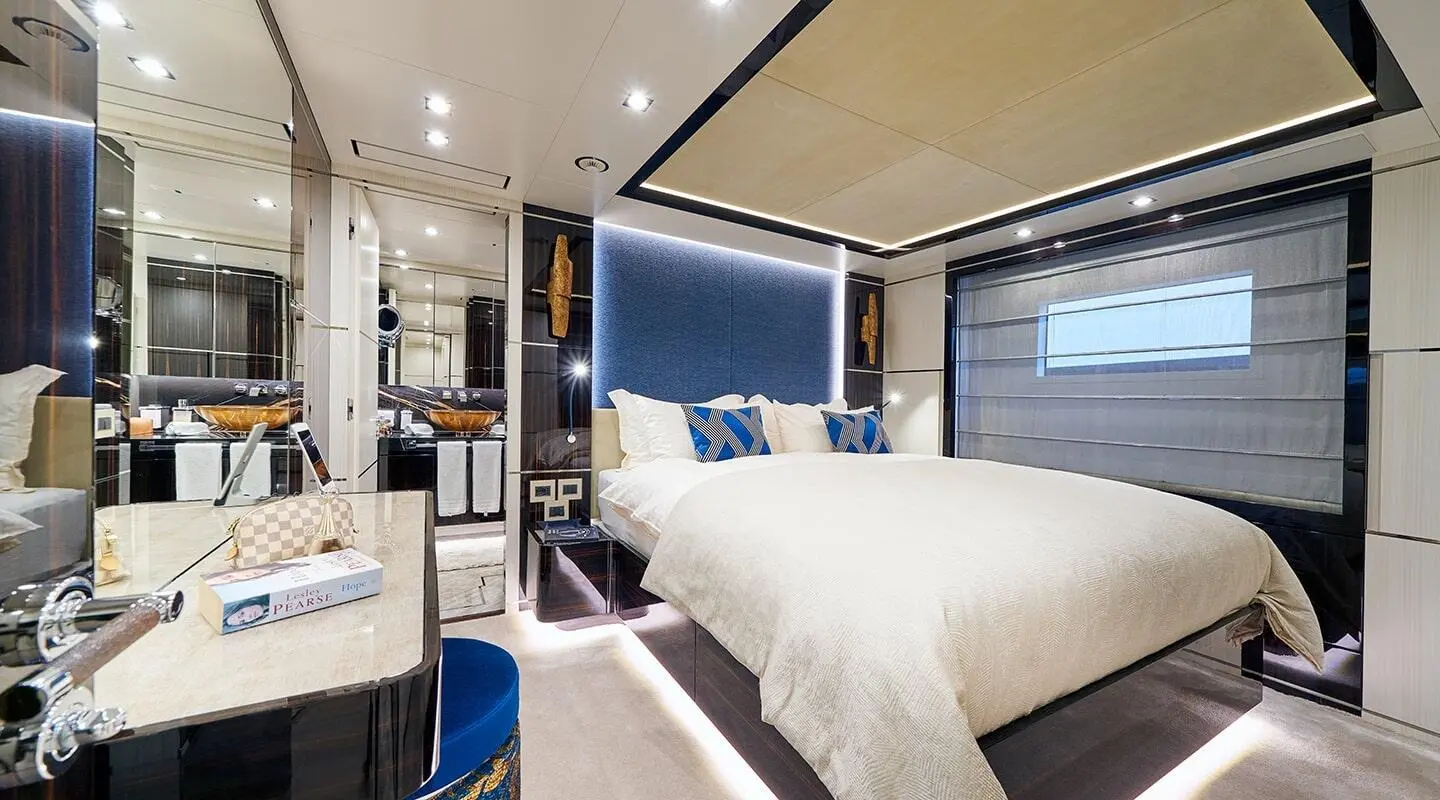 Luxurious yacht bedroom with large bed, blue accents, and warm lighting at sunset