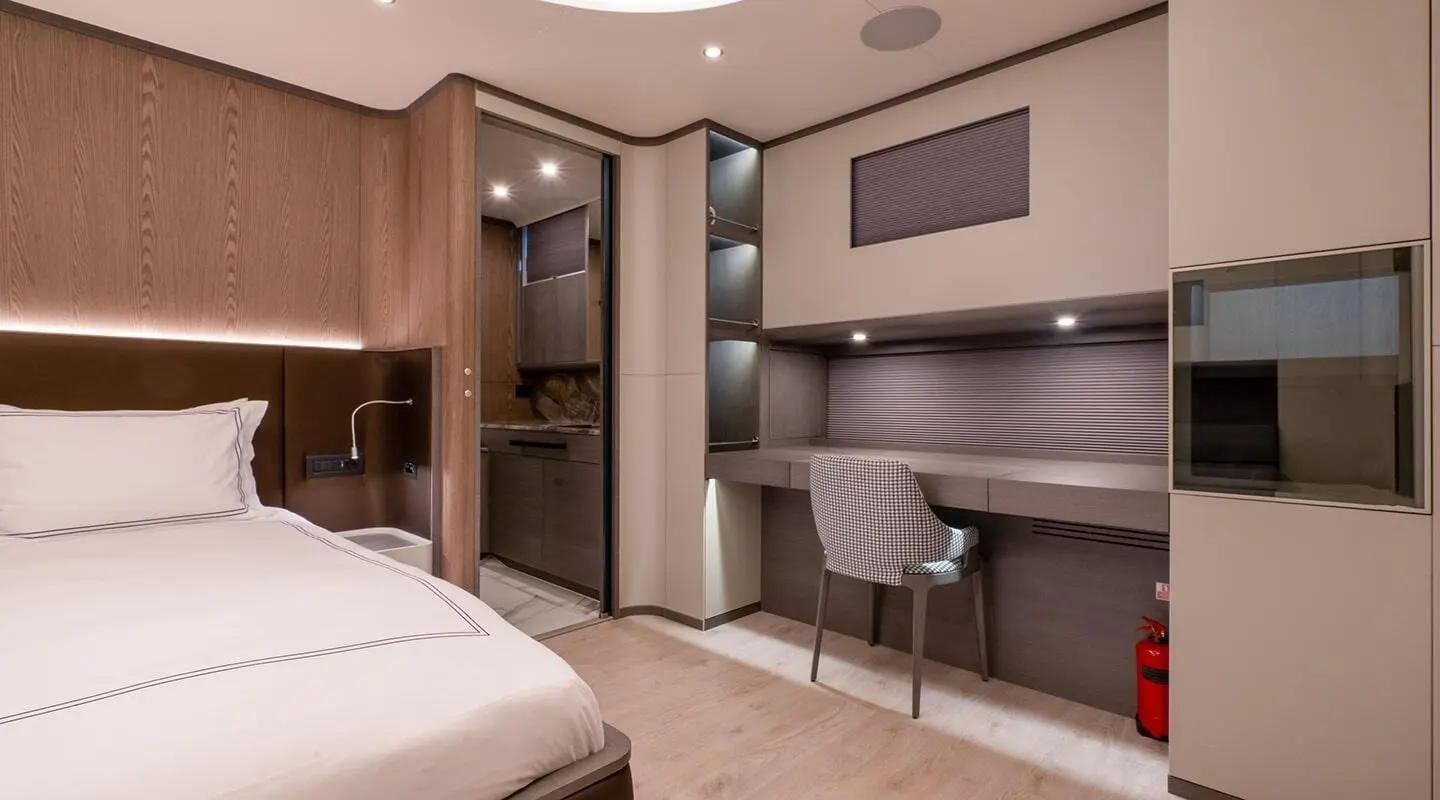Interior view of a yacht cabin with bed, desk, seating, and wooden cabinetry at dusk