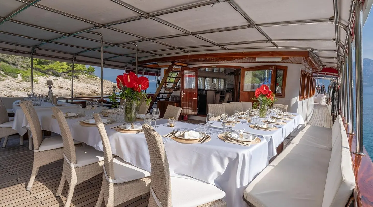 Elegant yacht Barbara dining area with white tablecloths, flowers, and sunset light