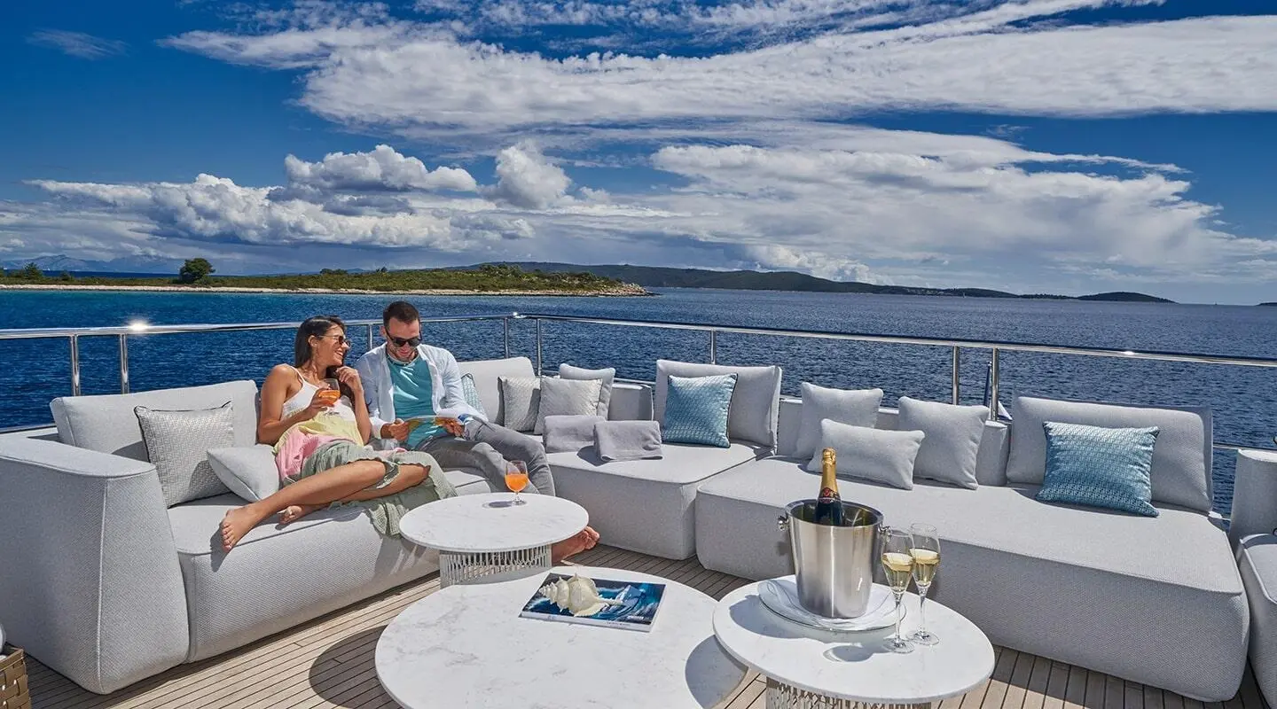 Aluminia Too yacht deck with seating, round tables, and sunset sea view