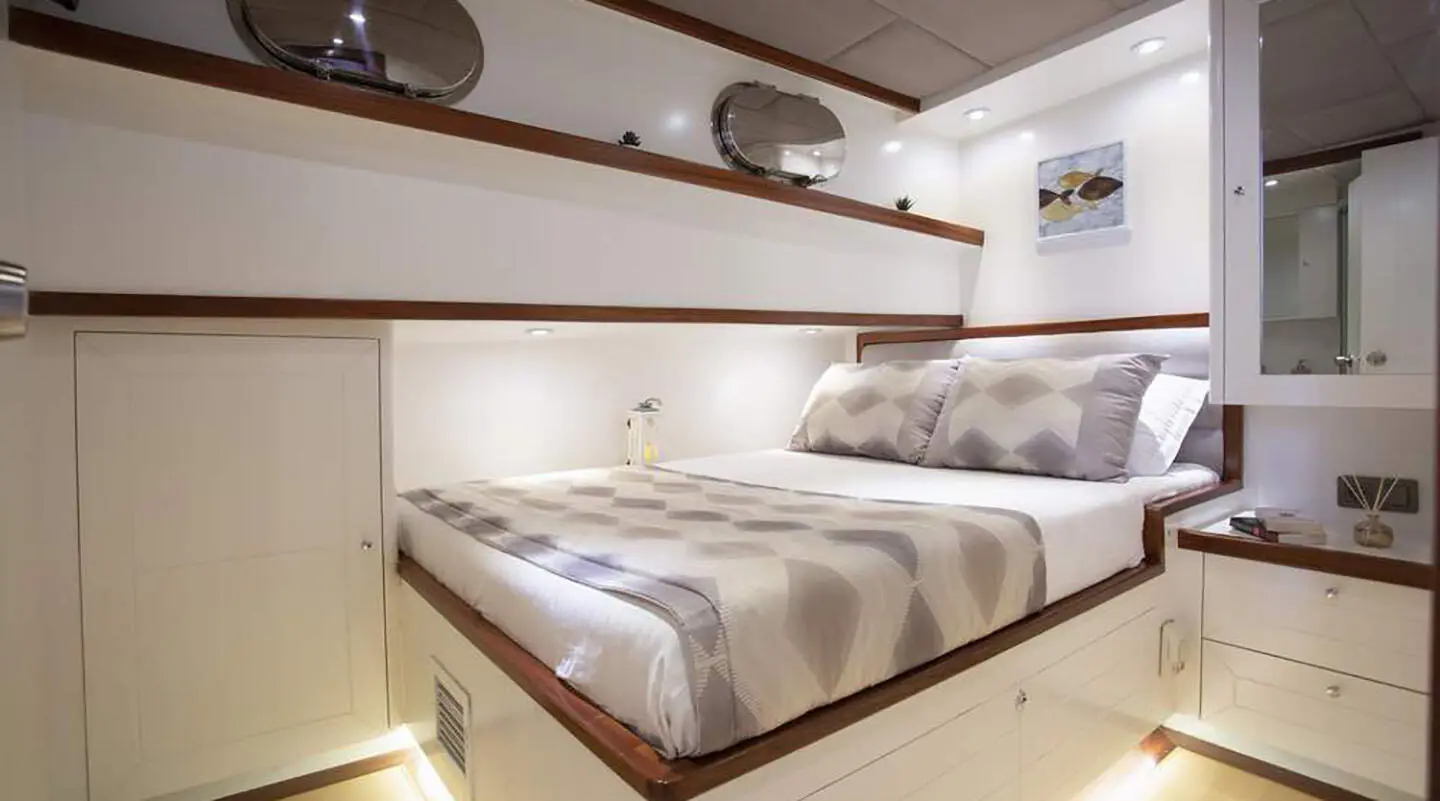 Luxurious yacht cabin with double bed, striped bedding and built-in shelves