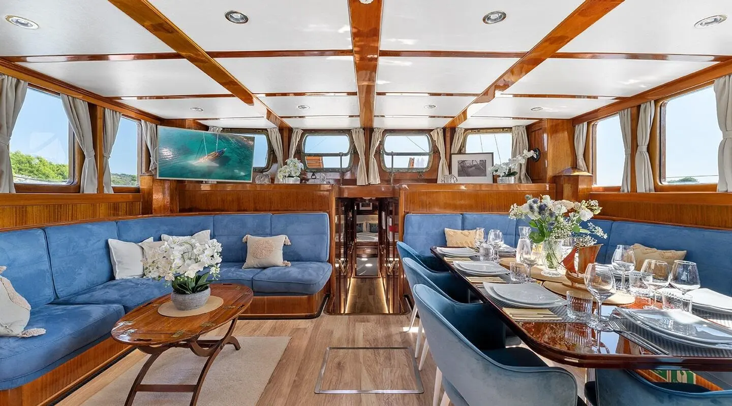 Luxury sailing yacht interior with wooden beams, seating, and dining tables at sunset