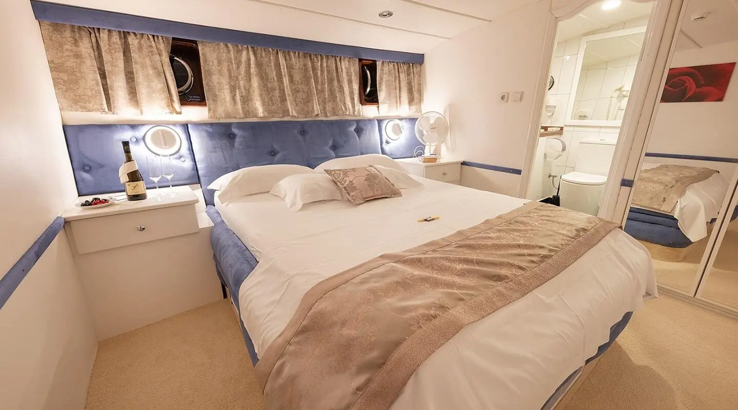 Aurum yacht bedroom with two twin beds, beige bedding, and blue headboard panel