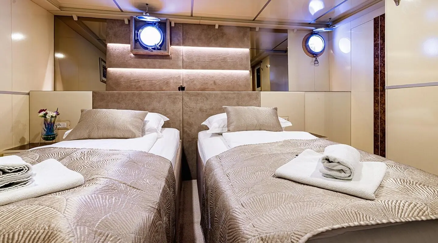 Interior of Melody yacht with twin beds, beige linens, and overhead lighting