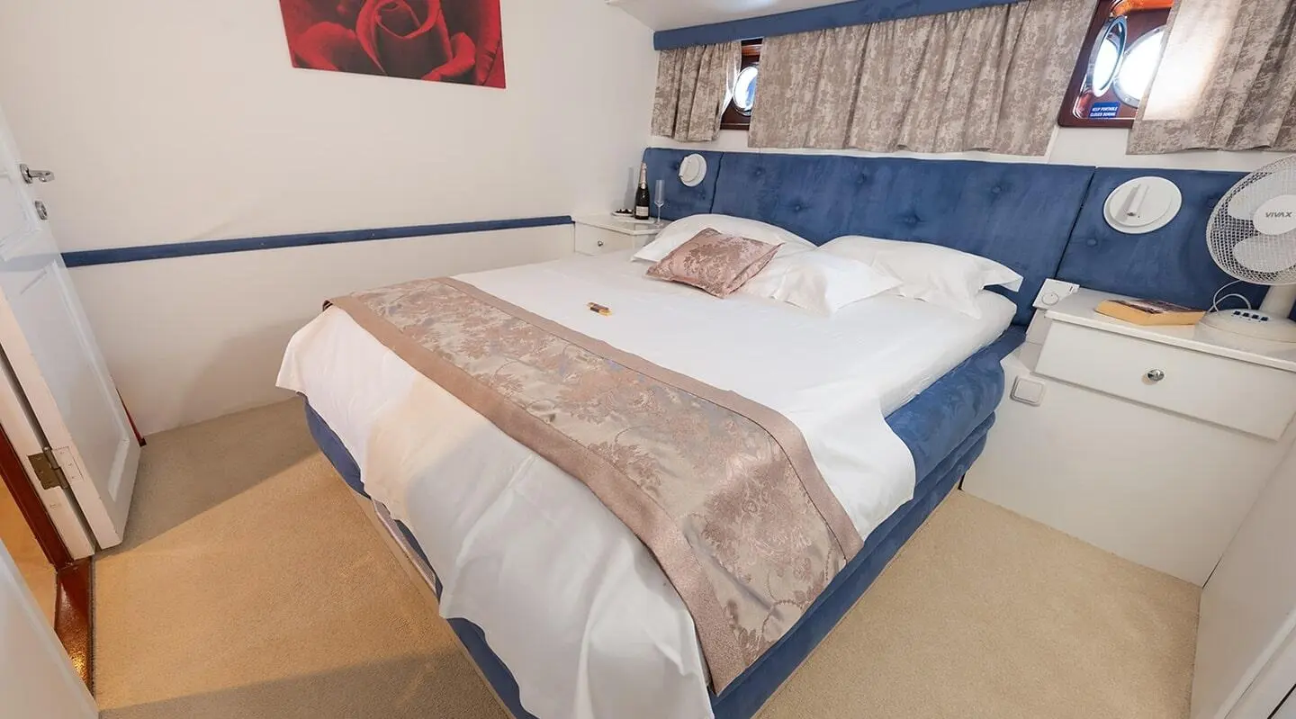 Arum yacht cabin with blue padded headboard, white bed, and beige blanket