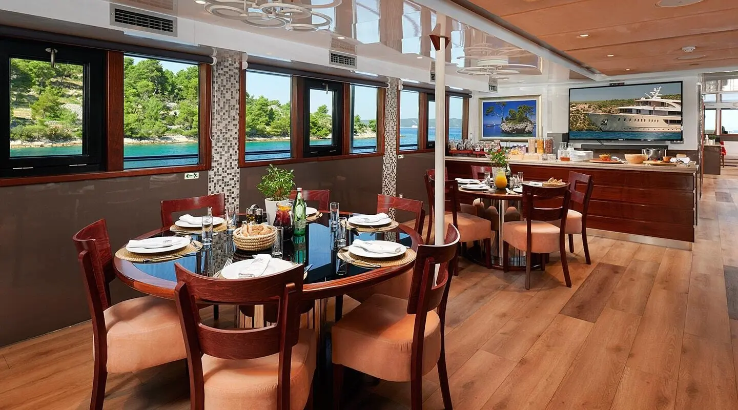Queen Eleganza yacht dining area on deck with wooden chairs and sunset view