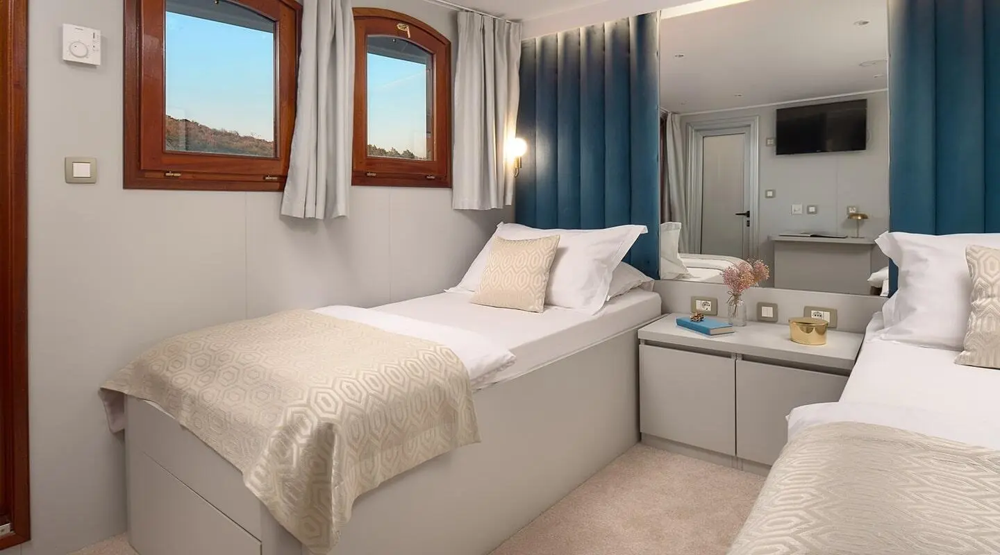 Bellezza yacht bedroom with two single beds, windows, and bedside table