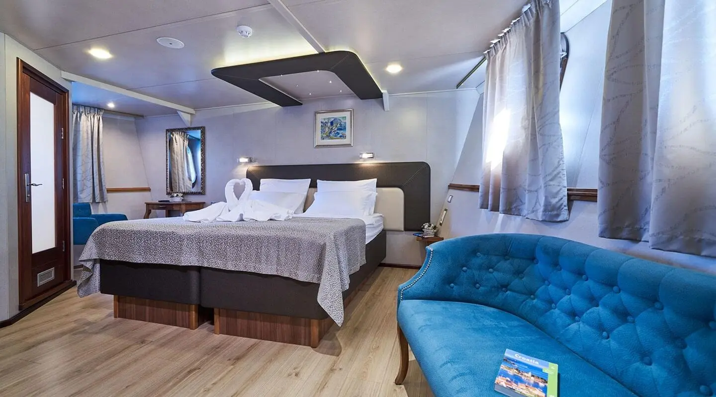 Casablanca yacht stateroom with large bed, nightstands, and blue seating area near window