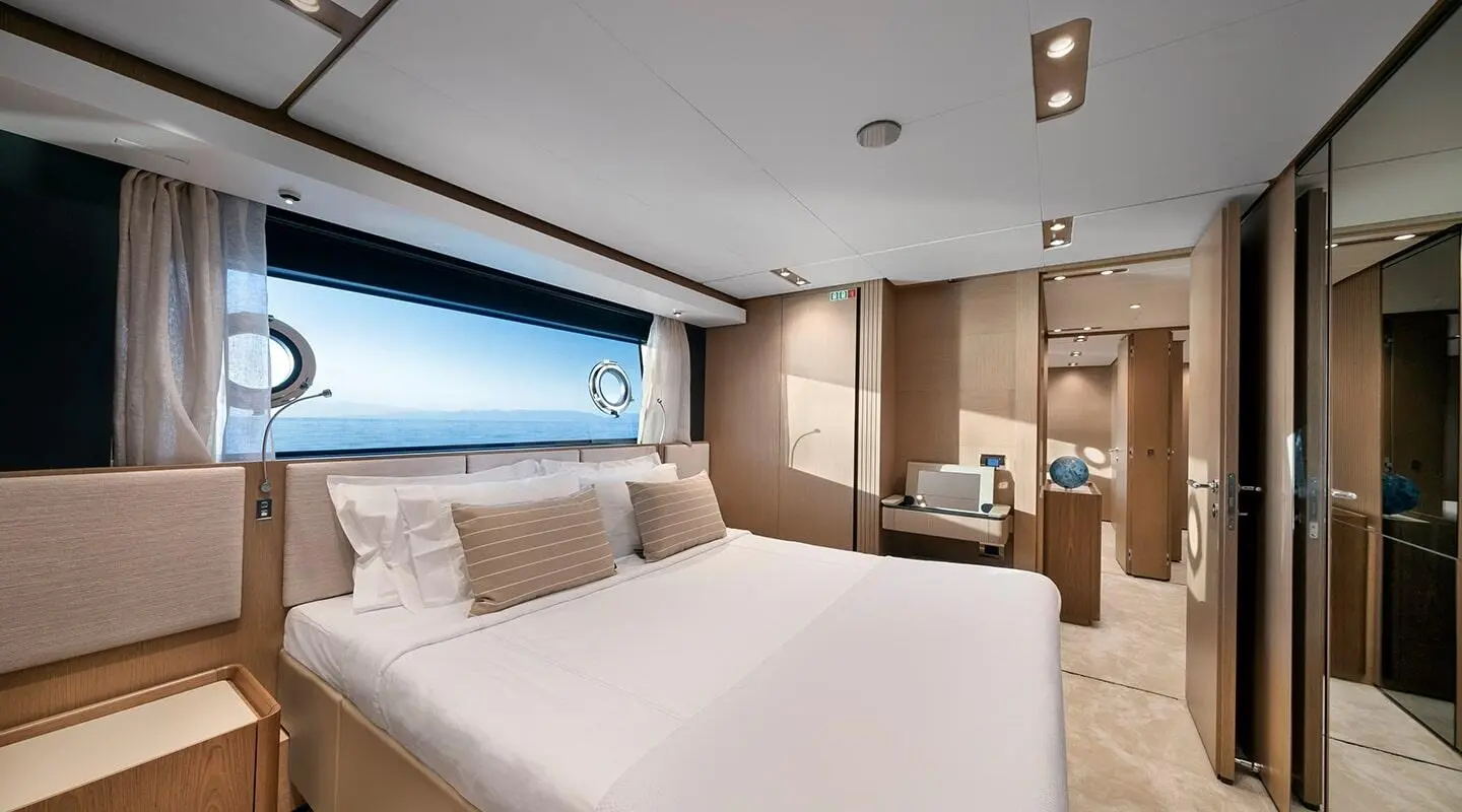 Spica yacht stateroom with large bed, beige cushions, and sea view through window