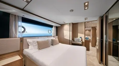 Spica yacht stateroom with large bed, beige cushions, and sea view through window