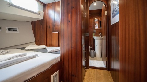Wood-paneled yacht cabin with a bed, towels, and a hallway leading to a bathroom