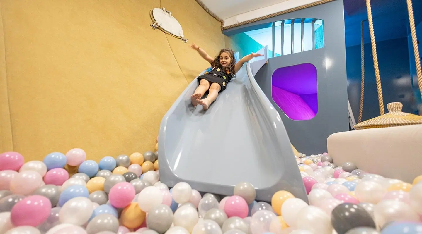 Bella yacht playscape slide with a child sliding into a ball pit.