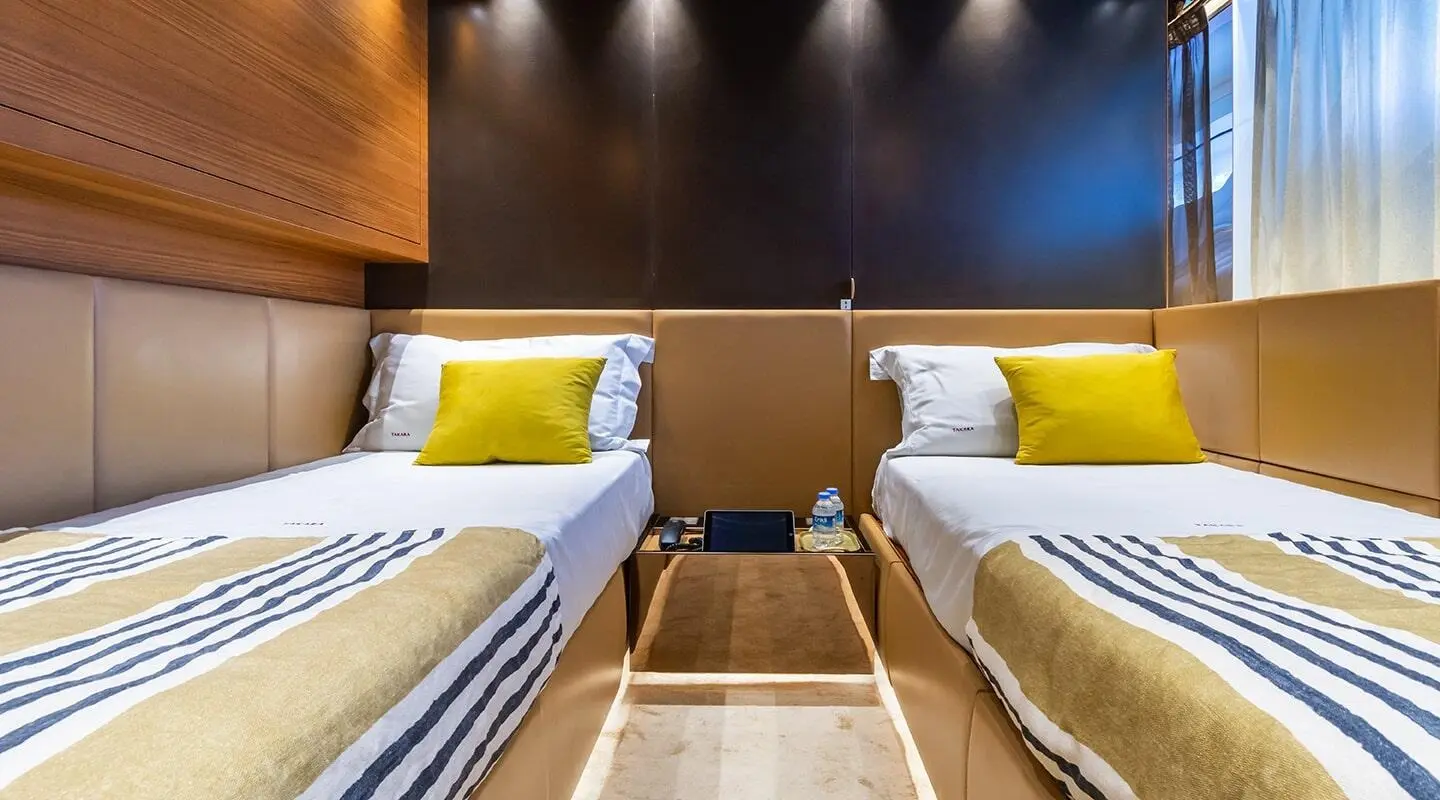Two twin beds in a bright yacht cabin with yellow cushions and bedside lamps
