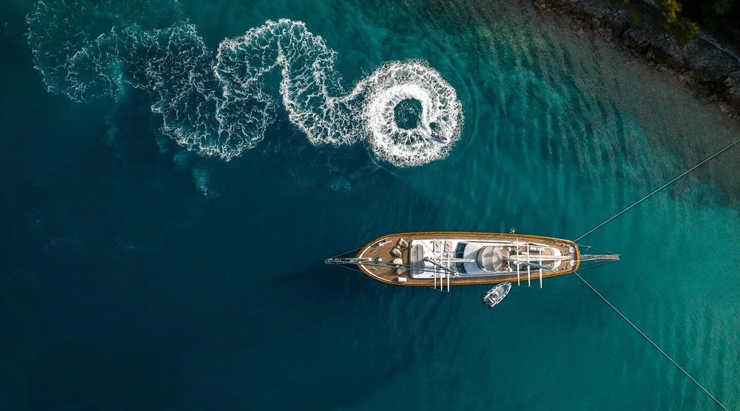 A luxury gulet anchored in turquoise sea at sunset with a small wooden boat nearby