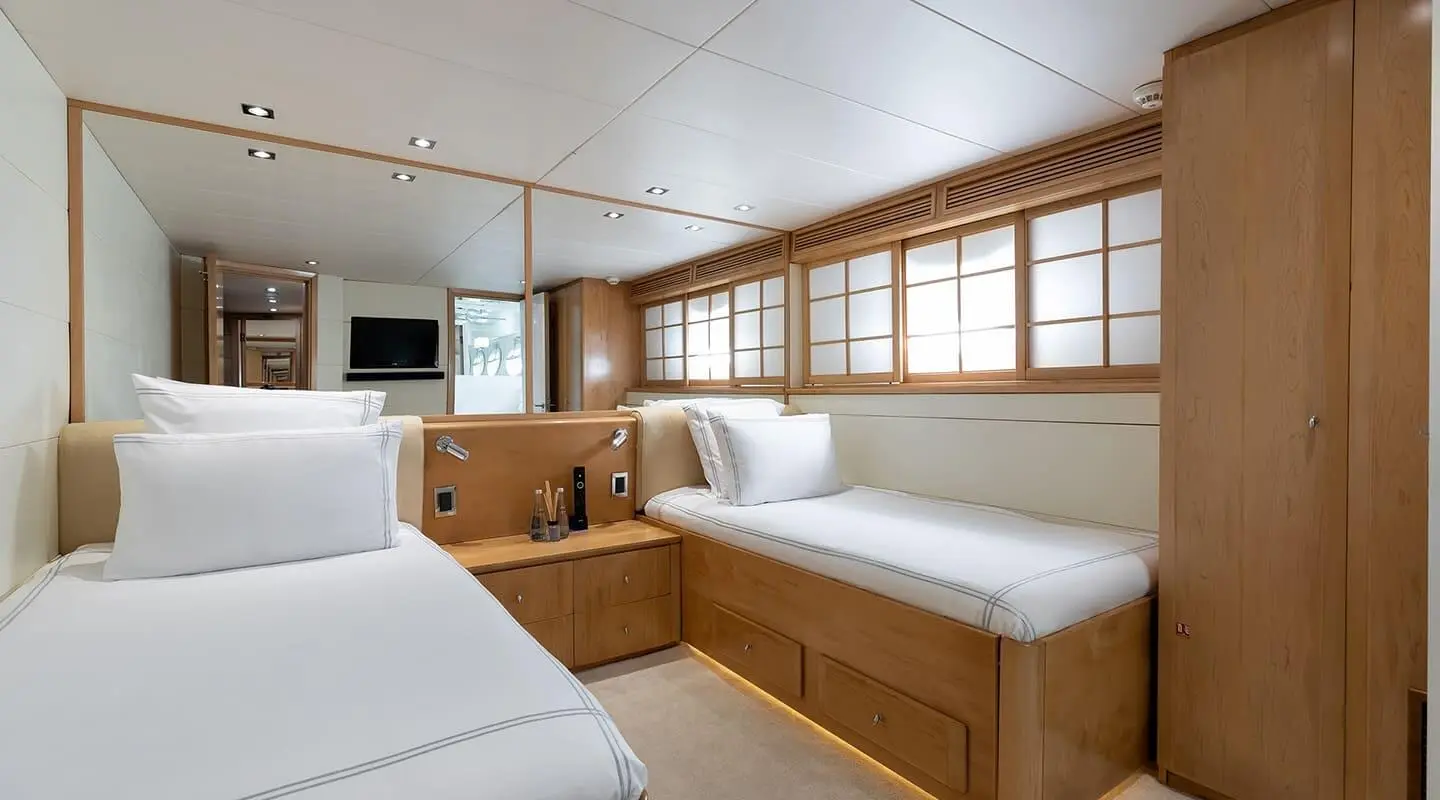 Two twin beds in a luxury yacht cabin with wooden cabinets and white pillows