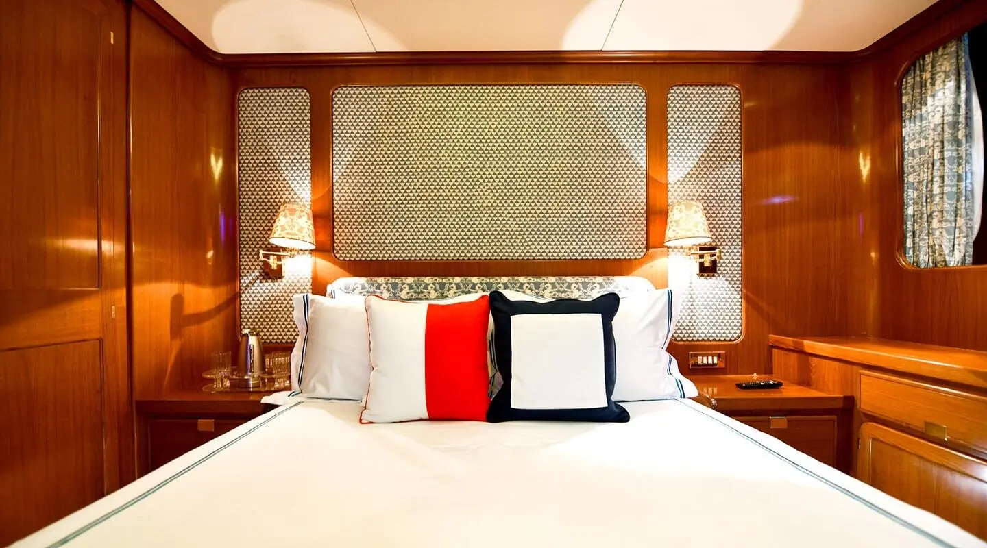 Tamarita yacht bedroom with wood headboard, white bedding and red/black pillows