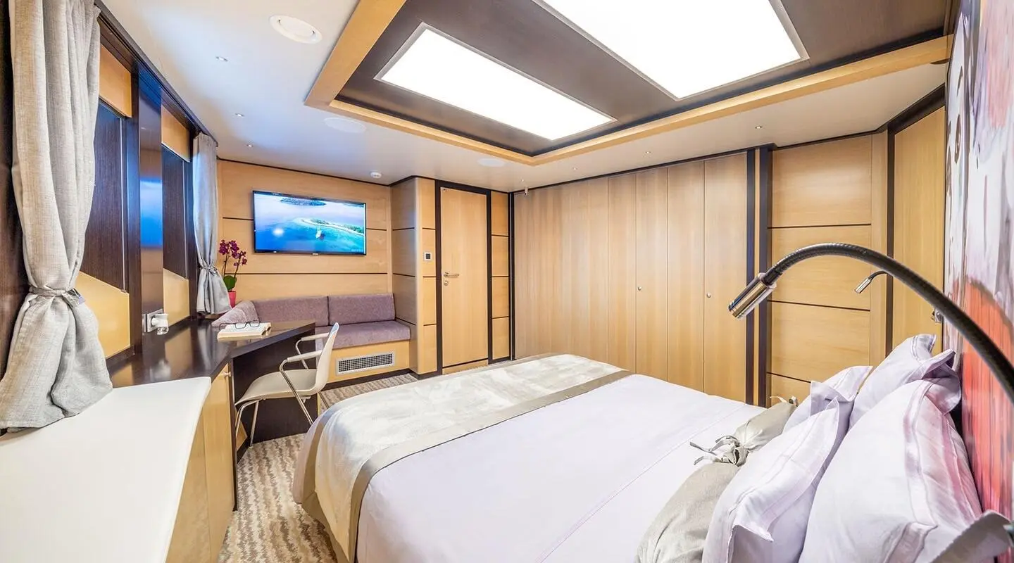 Navilux yacht interior with a neatly made bed, wood panels, and a TV