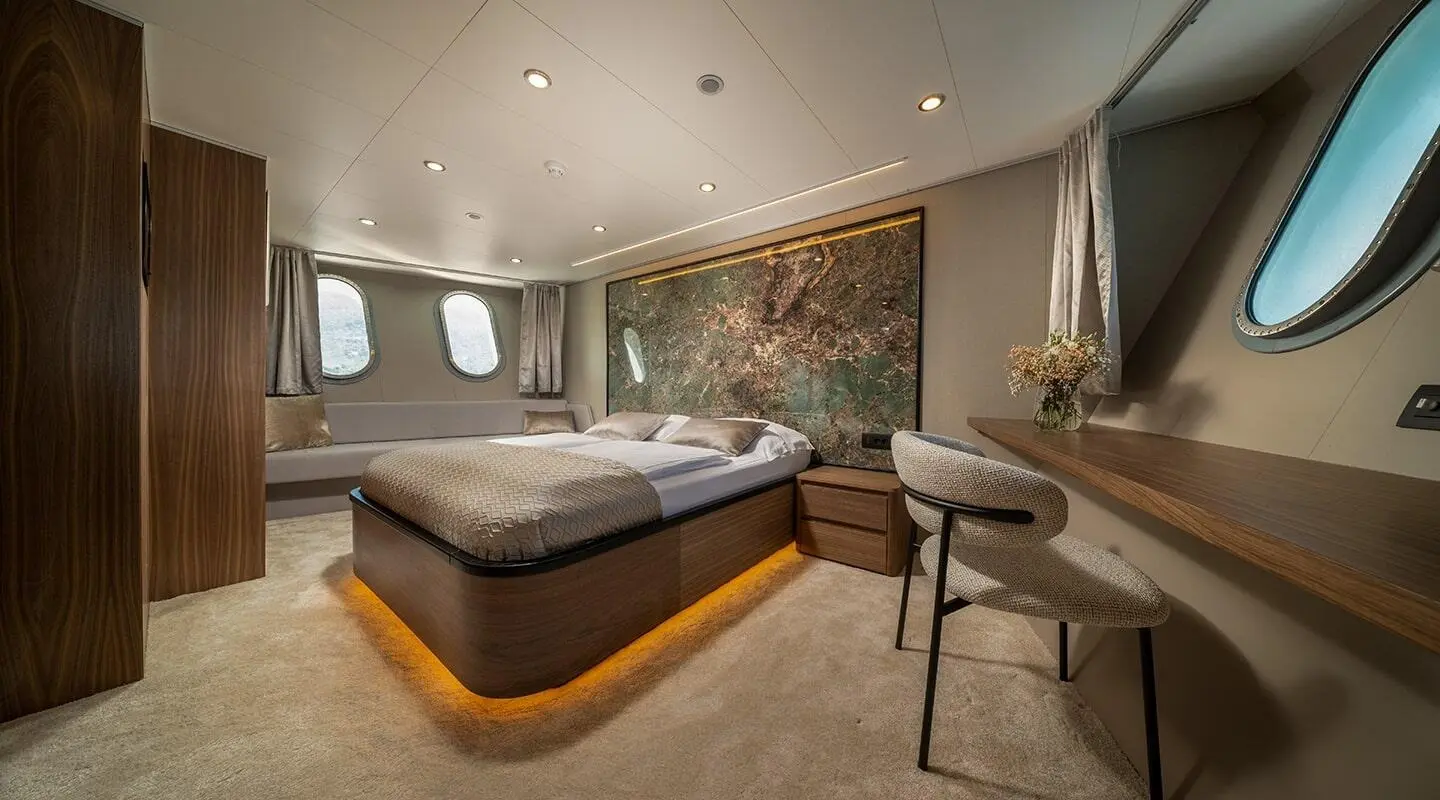 Interior bedroom with bed, desk, windows, and wall art in a yacht cabin