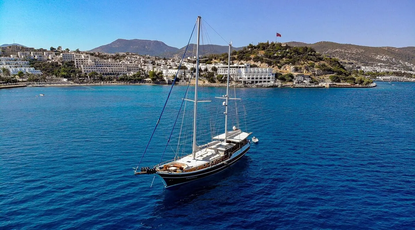 Wooden sailing yacht anchored in open blue sea, visible deck area