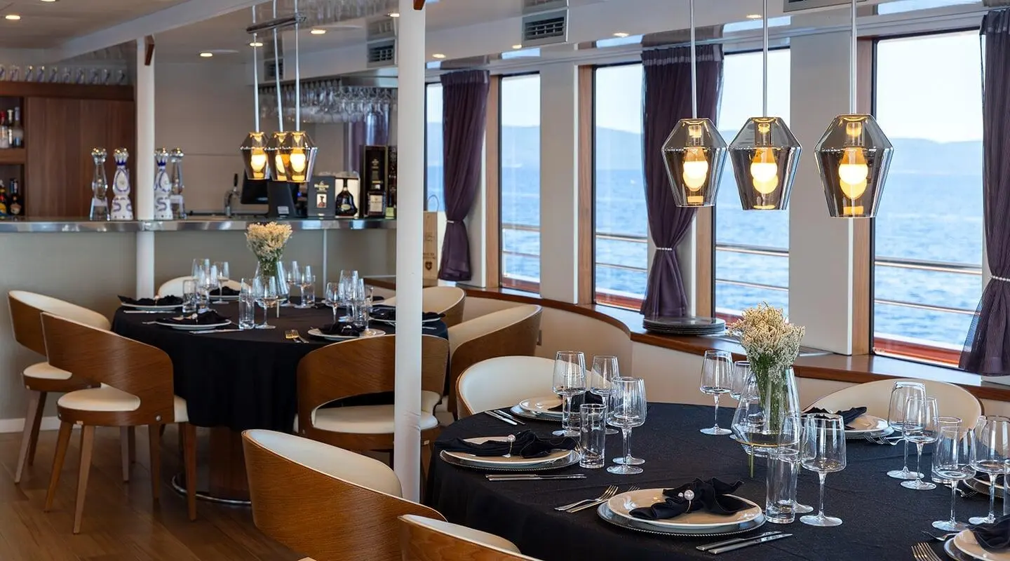 Interior seating and dining area of Yolo yacht, polished wood, large windows