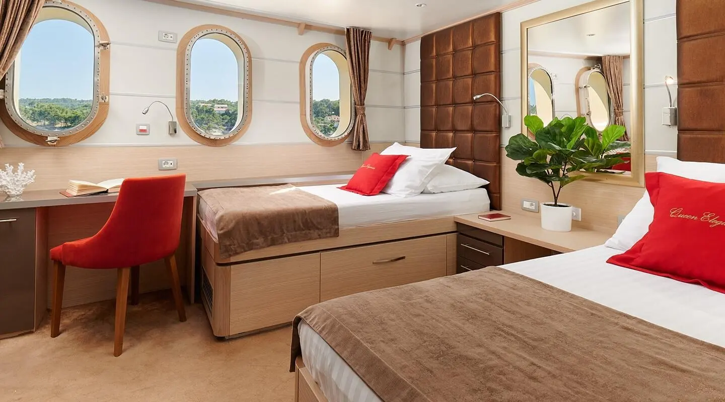 Queen Eleganza yacht interior with two brown beds, windows, and potted plant