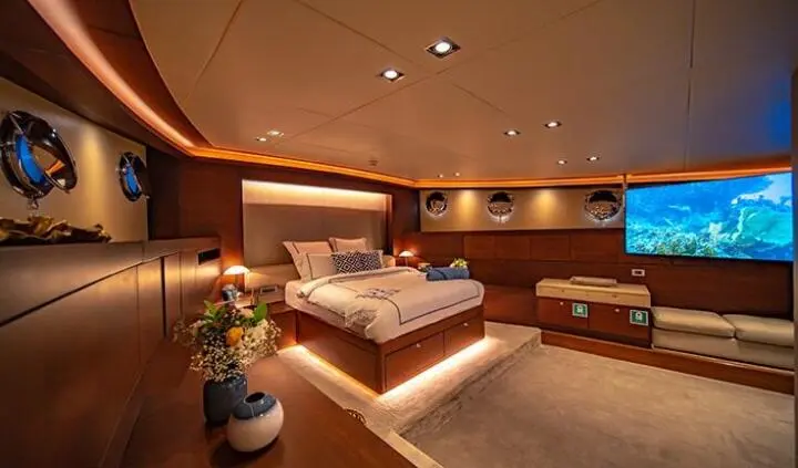 Interior cabin of a yacht with a large bed, wood panels, and ambient lighting