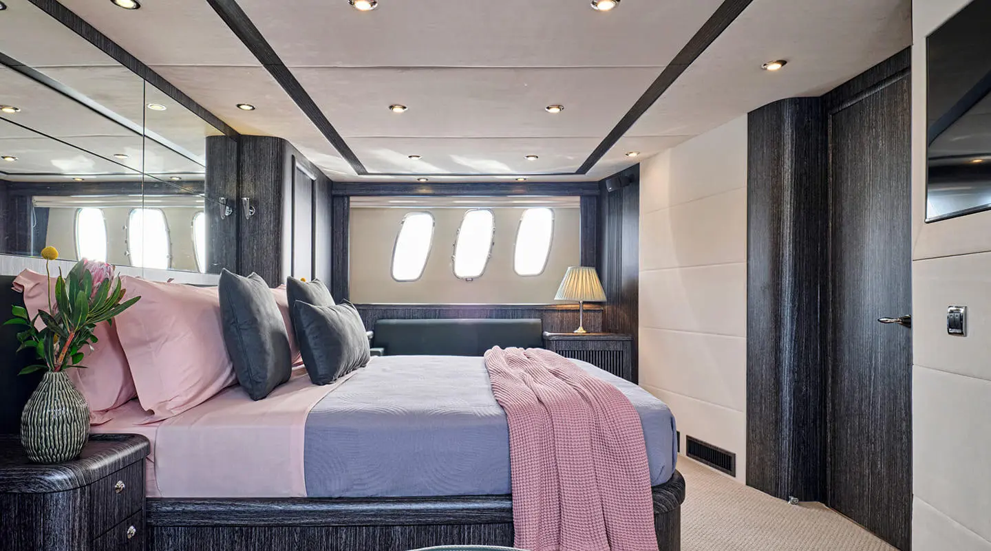 M Five yacht cabin with large bed, dark blue bedding, and windowed portholes