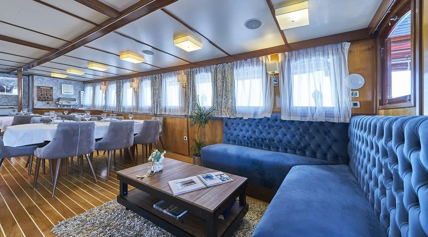 Interior lounge of Amorena yacht with blue seating and windows, stylized wood table