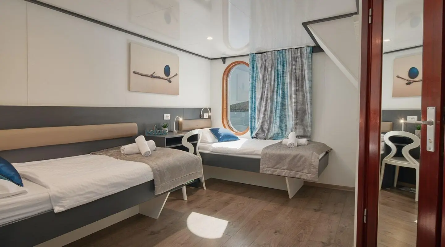 Lupus Mare yacht interior with two single beds, blue curtains, and nightstand