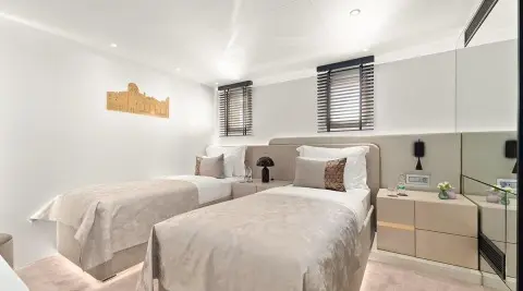 Two side-by-side twin beds in a bright yacht cabin with beige bedding and white walls