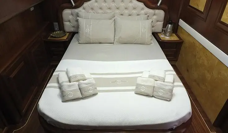 Queen bed in master cabin with two pillows and folded towels at foot