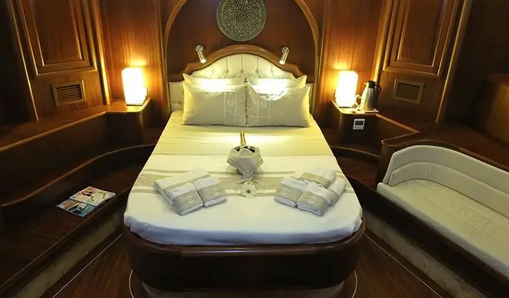 Master cabin with king bed, white linens, bedside lamps, and wooden panels