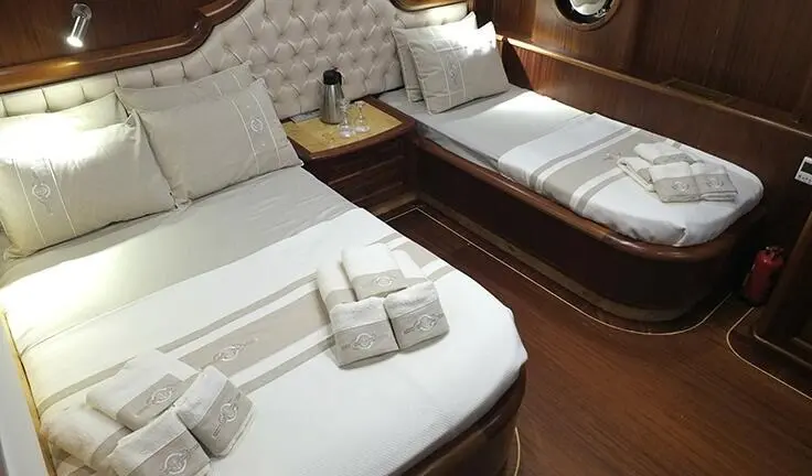 Twin cabin with two single beds, wooden bedside tables, and folded towels