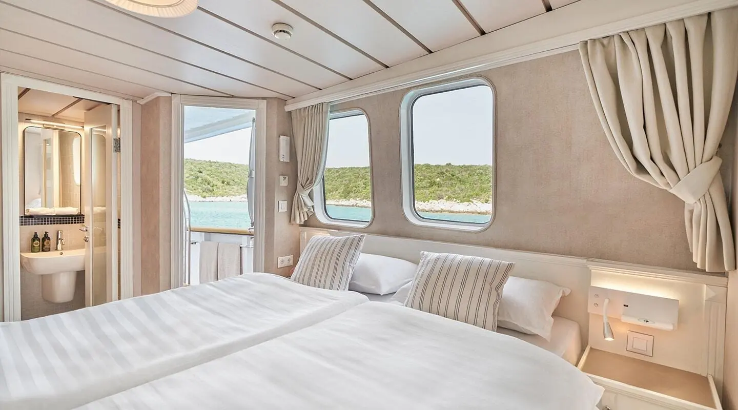 Bedroom aboard La Perla yacht with large bed, windows, and view