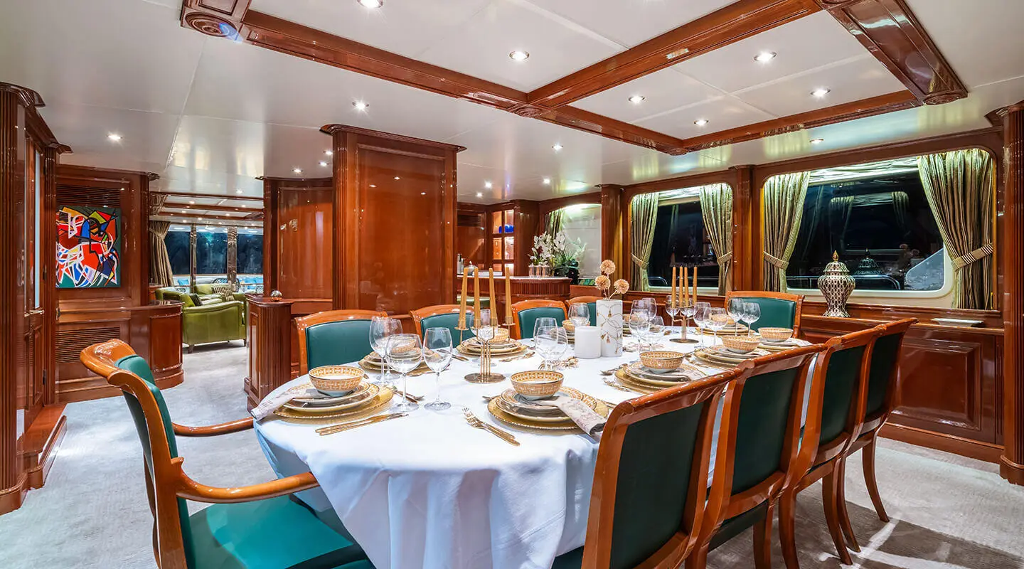 Amadea yacht dining area with round table set for meal and wooden chairs