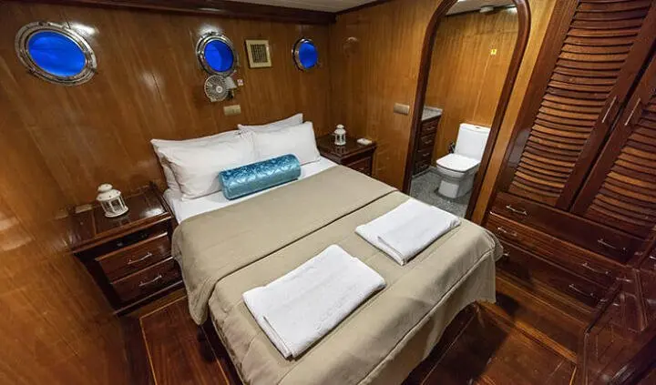 Master cabin with two single beds pushed together, white linens, wood panels, and rolled towels