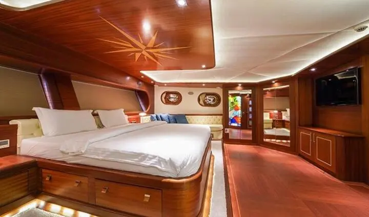 Master cabin with king bed, wooden walls, porthole, and ensuite bathroom visible