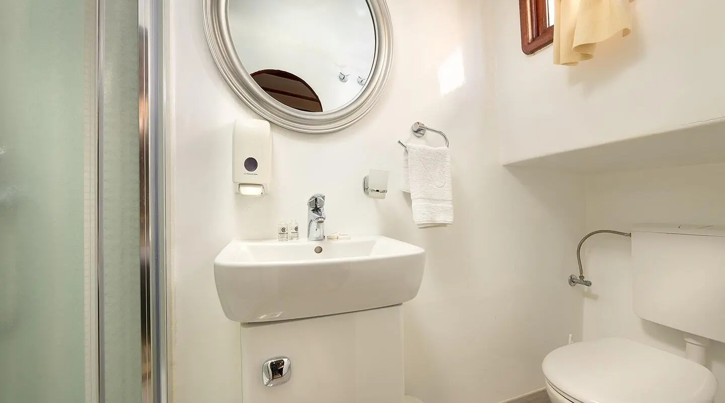 Linda yacht bathroom interior with white sink, round mirror, towel, and toilet