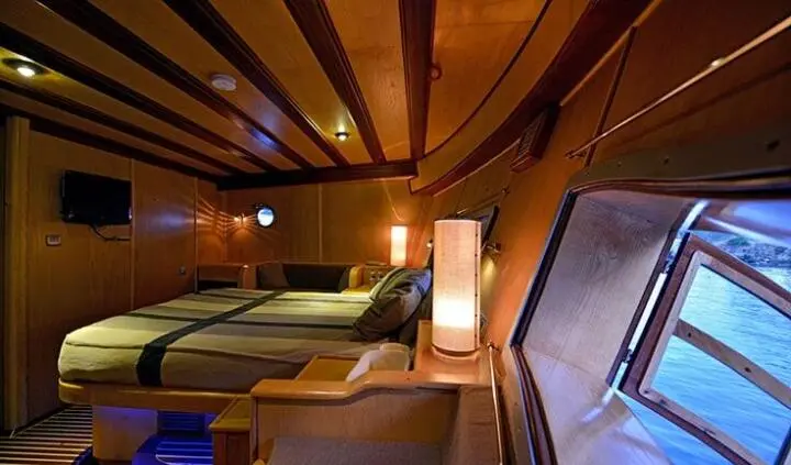 Cozy master cabin on a yacht with wooden beams, bed, and seating area