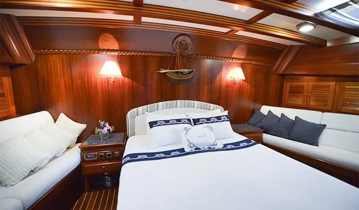Master cabin with king bed and wood paneling, bedside lamps, and porthole windows