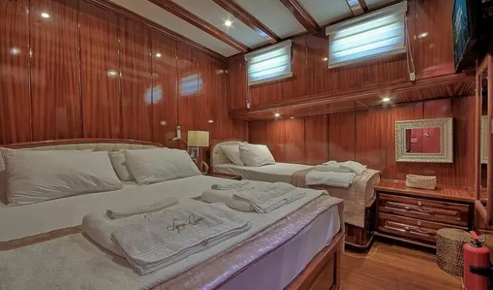 Lycian Queen cabin interior with two single beds, wood paneling, and soft lighting