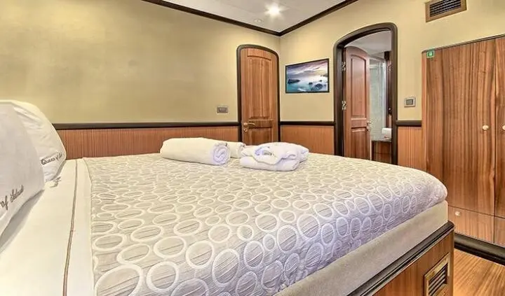 Queen Of Salmakis cabin with two twin beds, wooden wardrobe, and patterned bedding