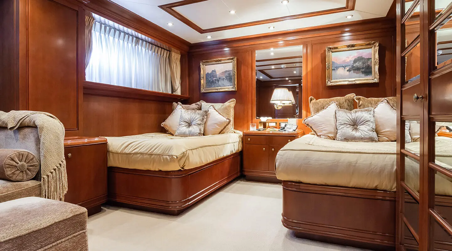 Apogee yacht deck interior with two beige beds and wooden cabinetry