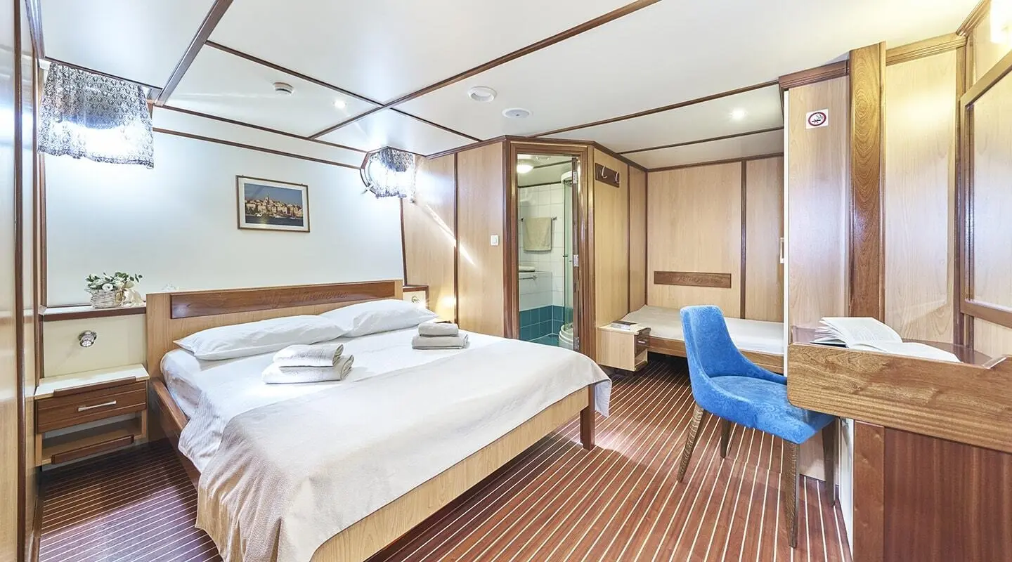 Interior of Amorena yacht bedroom with king bed, wooden panels, and seating